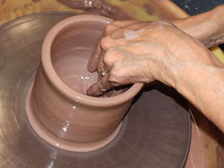 a photo showing two hands forming a pottery piece at a potters wheel