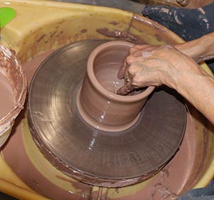 a photo showing the hands of a potter at the potters wheel