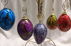 a photo of five gourds turned into colorful, hand-painted ornaments hanging by gold-colored ornament caps