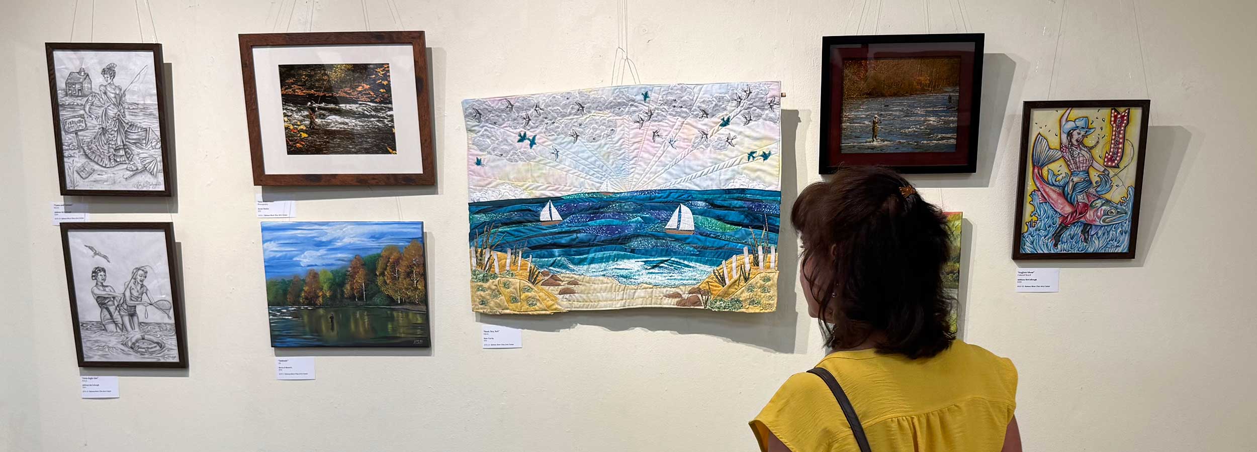 photo showing a woman looking at exhibits from the Hooked on Salmon River Art Show 2025