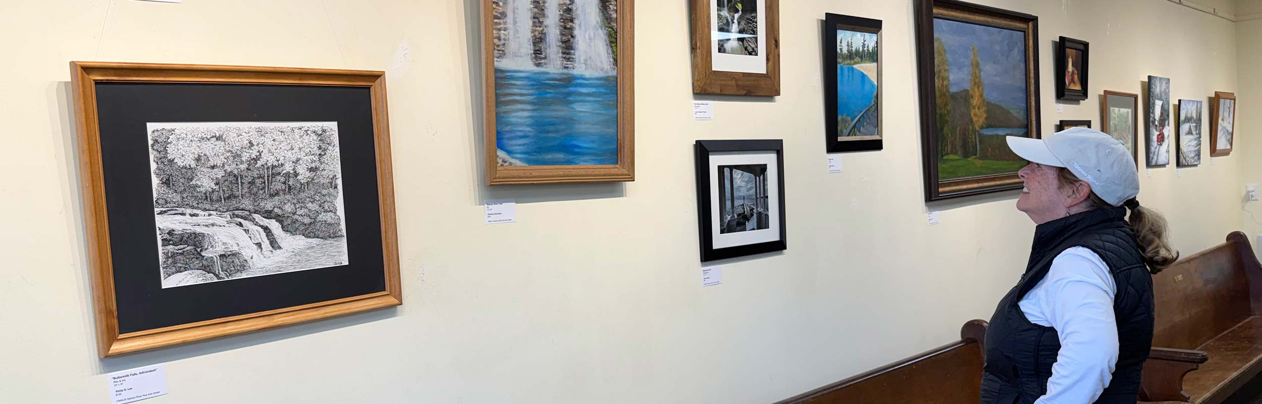 banner for the Arts Center Fall-Winter Show 2025 - 2026 showing several pieces of artwork and someone admiring them