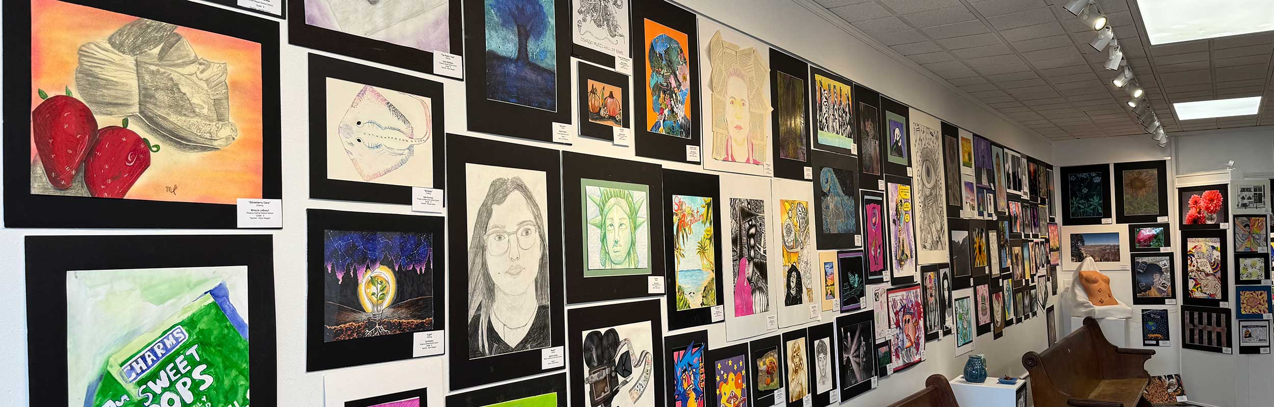 a photo of the Oswego County Student Art Show showing a long wall crowded with artworks by students
