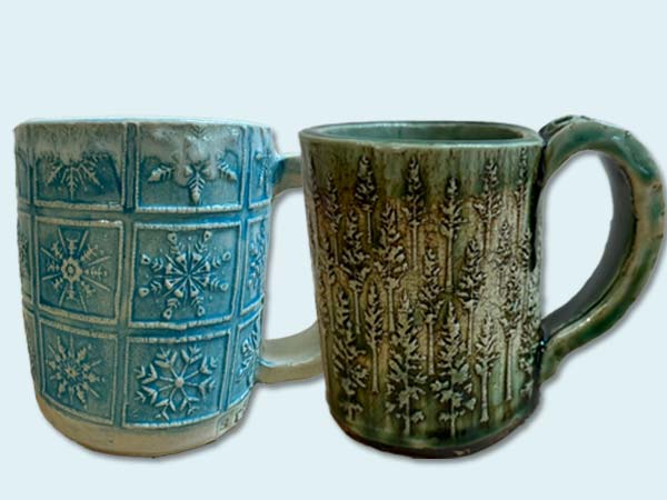 photo of two handmade mugs, one showing snowflakes and the other showing trees